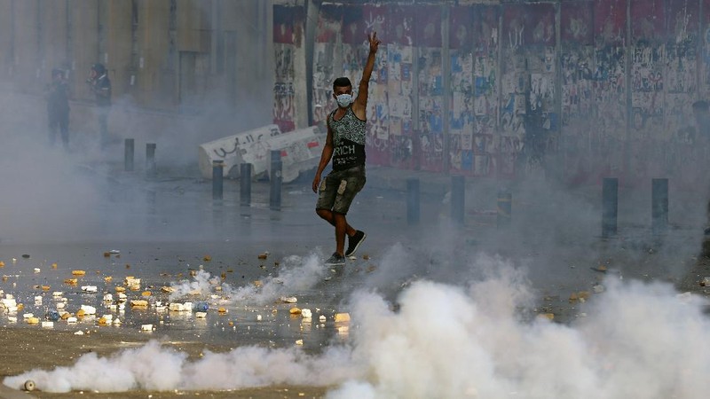 An anti-government protester flashes the victory sign amid tear gas fired by riot police during a protest marking the first anniversary of the massive blast at Beirut's port, near Parliament Square, In Beirut, Lebanon, Wednesday, Aug. 4, 2021. United in grief and anger, families of the victims and other Lebanese came out into the streets of Beirut on Wednesday to demand accountability as banks, businesses and government offices shuttered to mark one year since the horrific explosion. (AP Photo/Bilal Hussein)