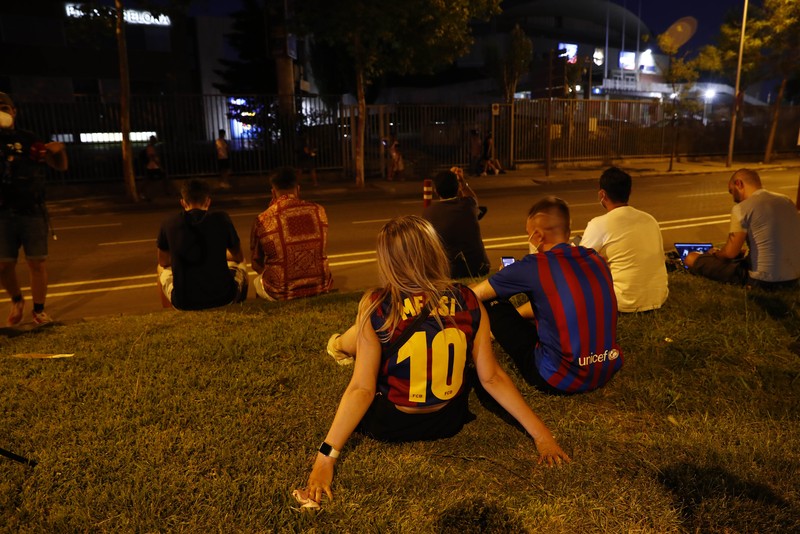 Spain Soccer Barcelona Messi A fan wearing the number 10 Lionel Messi replica shirt sits outside the club offices with others in Barcelona, Spain, Thursday, Aug. 5, 2021. Barcelona announced Thursday that Messi will not stay with the club, saying that the Spanish league's financial regulations made it impossible to sign the Argentina star to a new contract. (AP Photo/Joan Monfort)