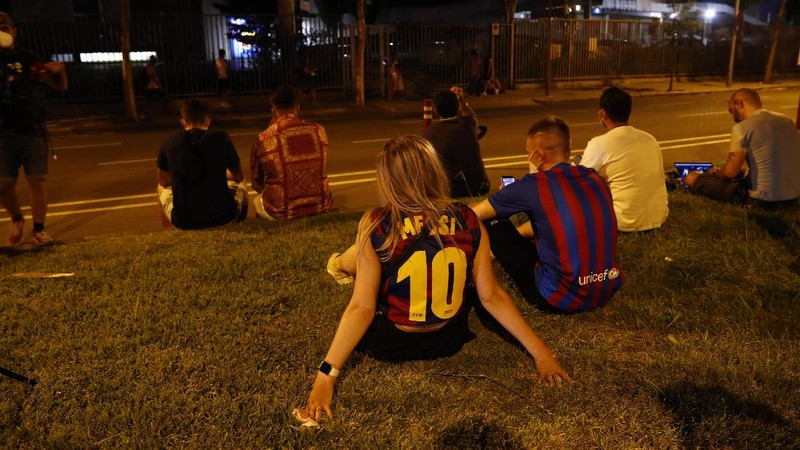 A fan wearing the number 10 Lionel Messi replica shirt sits outside the club offices with others in Barcelona, Spain, Thursday, Aug. 5, 2021. Barcelona announced Thursday that Messi will not stay with the club, saying that the Spanish league's financial regulations made it impossible to sign the Argentina star to a new contract. (AP Photo/Joan Monfort)