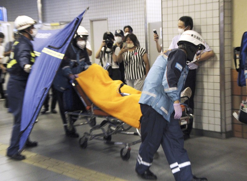 Penusukan di Tokyo Jepang Rescuers carry an injured passenger on stretcher at Soshigaya Okura Station after stabbing on a commuter train, in Tokyo Friday night, Aug. 6, 2021. A man with a knife attacked 10 passengers on a commuter train in Tokyo on Friday and was arrested by police after fleeing, fire department officials and news reports said. (Kyodo News via AP)