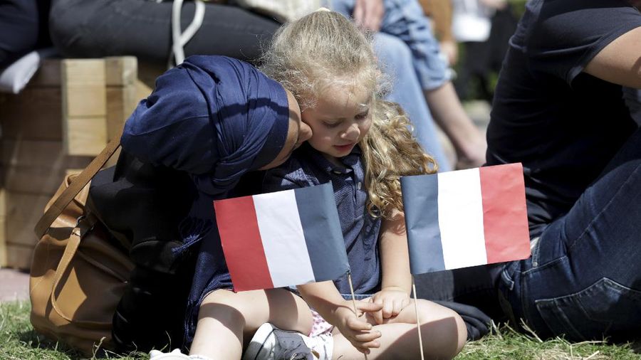 A woman speaks with a small girl holding French flags as they sit in the Olympics fan zone at the Trocadero Gardens in Paris, Sunday, Aug. 8, 2021. Celebrations were held in Paris Sunday as part of the handover ceremony of Tokyo 2020 to Paris 2024, as Paris will be the next Summer Games host in 2024. The passing of the hosting baton will be split between the Olympic Stadium in Tokyo and a public party and concert in Paris. (AP Photo/Adrienne Surprenant)