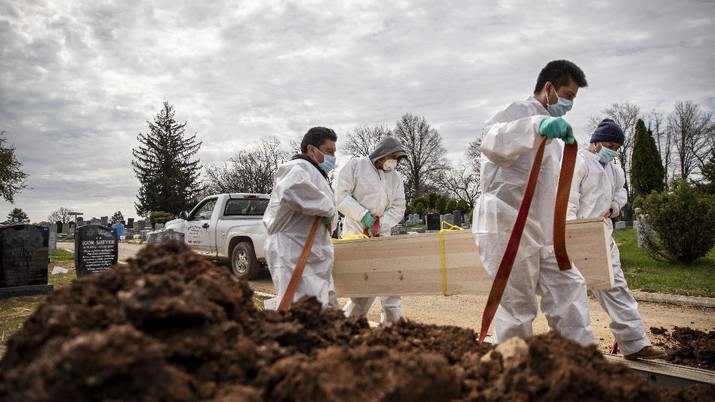 Pemakaman Covid-19 di New York (AP/David Goldman) Gravediggers carry the casket of someone presumed to have died from coronavirus as they are buried without any family present at Mount Richmond Cemetery in the Staten Island borough of New York, Tuesday, April 7, 2020. In a marathon of grief at this small Jewish cemetery mounds of dirt are piling up as graves are opened, vans are constantly arriving with bodies aboard and a line of white signs is being pressed into the ground marking plots soon to be occupied. Families are being kept away from their loved one's gravesite at the cemetery, which caters to those with little or nothing. (AP Photo/David Goldman)