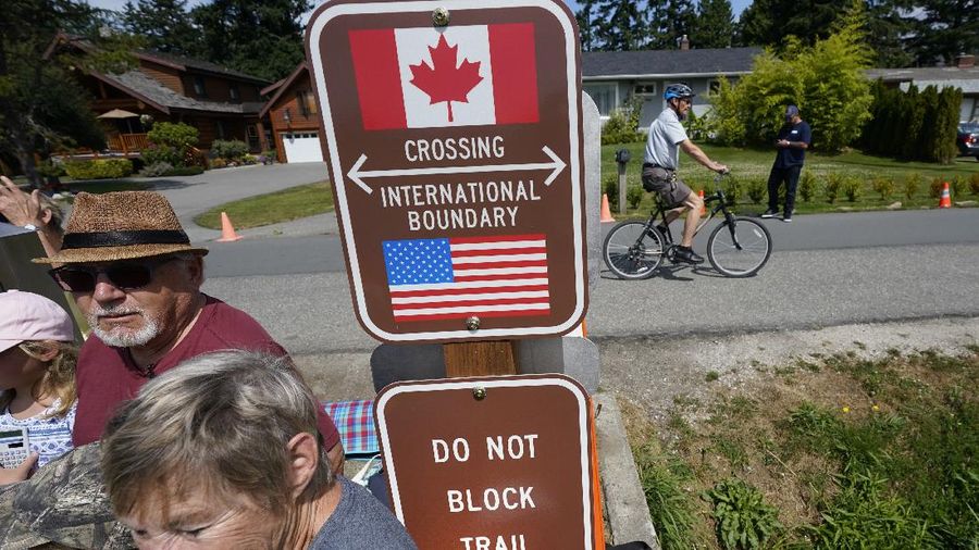 A family visits across the U.S.-Canada border at the Peace Arch Historical State Park as a cyclist rides past on the Canadian side, Monday, Aug. 9, 2021, in Blaine, Wash. Canada lifted its prohibition on Americans crossing the border to shop, vacation or visit but America kept similar restrictions in place, part of a bumpy return to normalcy from coronavirus travel bans. (AP Photo/Elaine Thompson)