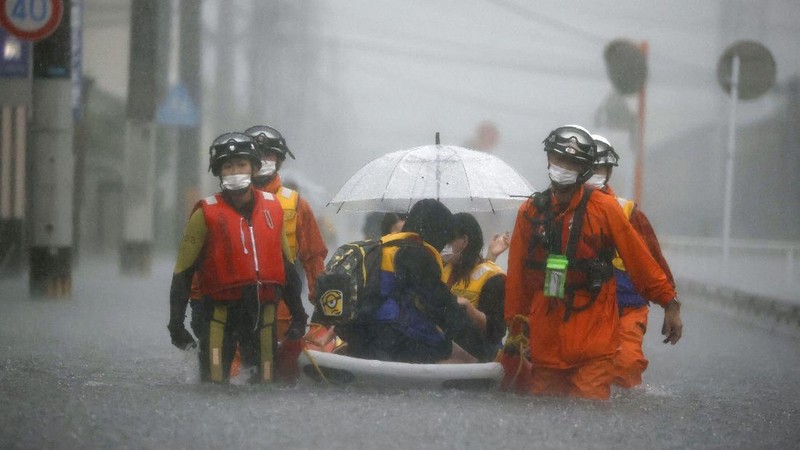 People wade through a road flooded by heavy rain in Kurume, Fukuoka prefecture, western Japan, Saturday, Aug. 14, 2021. Torrential rain pounding southwestern Japan triggered a mudslide early Friday that swallowed some people and was threatening to cause flooding and more landslides in the region. (Kyodo News via AP)