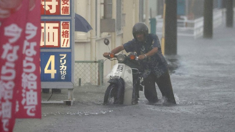 People wade through a road flooded by heavy rain in Kurume, Fukuoka prefecture, western Japan, Saturday, Aug. 14, 2021. Torrential rain pounding southwestern Japan triggered a mudslide early Friday that swallowed some people and was threatening to cause flooding and more landslides in the region. (Kyodo News via AP)
