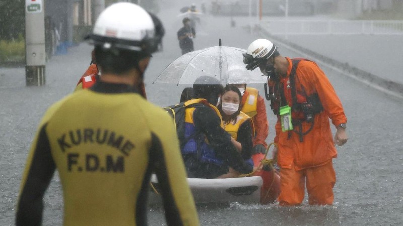 People wade through a road flooded by heavy rain in Kurume, Fukuoka prefecture, western Japan, Saturday, Aug. 14, 2021. Torrential rain pounding southwestern Japan triggered a mudslide early Friday that swallowed some people and was threatening to cause flooding and more landslides in the region. (Kyodo News via AP)