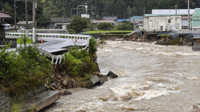 People wade through a road flooded by heavy rain in Kurume, Fukuoka prefecture, western Japan, Saturday, Aug. 14, 2021. Torrential rain pounding southwestern Japan triggered a mudslide early Friday that swallowed some people and was threatening to cause flooding and more landslides in the region. (Kyodo News via AP)