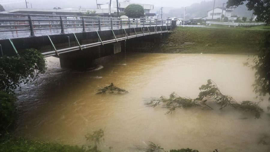 People wade through a road flooded by heavy rain in Kurume, Fukuoka prefecture, western Japan, Saturday, Aug. 14, 2021. Torrential rain pounding southwestern Japan triggered a mudslide early Friday that swallowed some people and was threatening to cause flooding and more landslides in the region. (Kyodo News via AP)