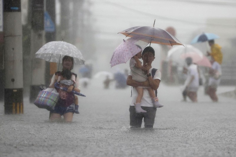 Japan Heavy Rain People wade through a road flooded by heavy rain in Kurume, Fukuoka prefecture, western Japan, Saturday, Aug. 14, 2021. Torrential rain pounding southwestern Japan triggered a mudslide early Friday that swallowed some people and was threatening to cause flooding and more landslides in the region. (Kyodo News via AP)