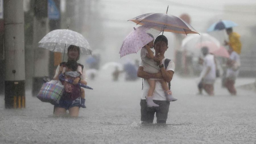 People wade through a road flooded by heavy rain in Kurume, Fukuoka prefecture, western Japan, Saturday, Aug. 14, 2021. Torrential rain pounding southwestern Japan triggered a mudslide early Friday that swallowed some people and was threatening to cause flooding and more landslides in the region. (Kyodo News via AP)