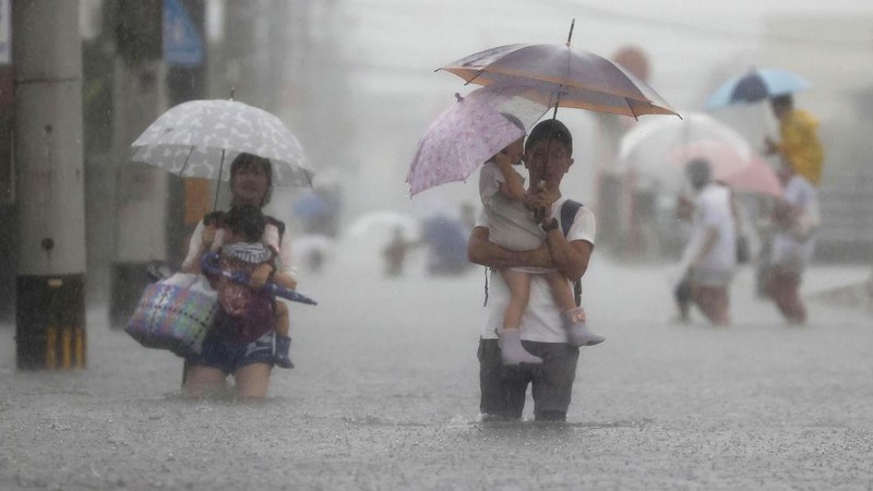 People wade through a road flooded by heavy rain in Kurume, Fukuoka prefecture, western Japan, Saturday, Aug. 14, 2021. Torrential rain pounding southwestern Japan triggered a mudslide early Friday that swallowed some people and was threatening to cause flooding and more landslides in the region. (Kyodo News via AP)