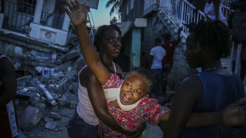 People walk past a home destroyed by the earthquake in Les Cayes, Haiti, Saturday, Aug. 14, 2021. A 7.2 magnitude earthquake struck Haiti on Saturday, with the epicenter about 125 kilometers (78 miles) west of the capital of Port- au-Prince, the US Geological Survey said. (AP Photo/Joseph Odelyn)