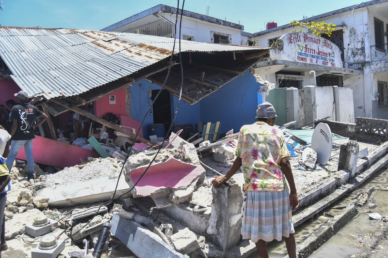 People walk past a home destroyed by the earthquake in Les Cayes, Haiti, Saturday, Aug. 14, 2021. A 7.2 magnitude earthquake struck Haiti on Saturday, with the epicenter about 125 kilometers (78 miles) west of the capital of Port- au-Prince, the US Geological Survey said. (AP Photo/Joseph Odelyn)