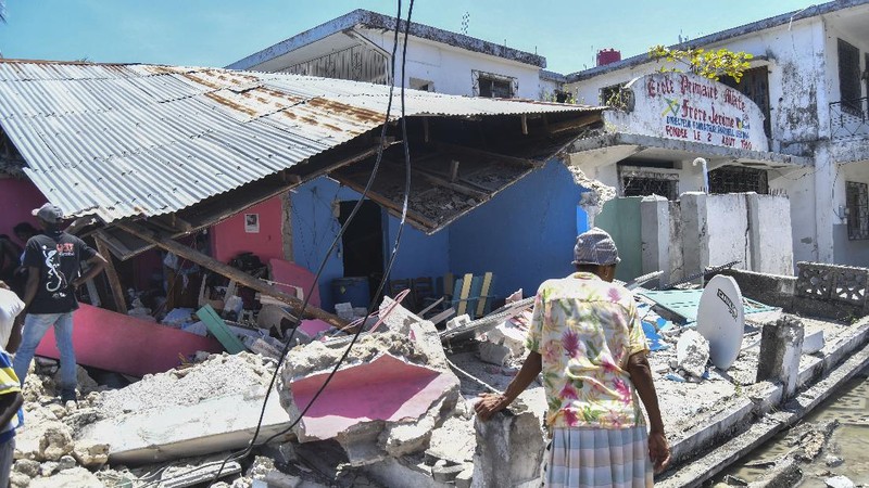 People walk past a home destroyed by the earthquake in Les Cayes, Haiti, Saturday, Aug. 14, 2021. A 7.2 magnitude earthquake struck Haiti on Saturday, with the epicenter about 125 kilometers (78 miles) west of the capital of Port- au-Prince, the US Geological Survey said. (AP Photo/Joseph Odelyn)