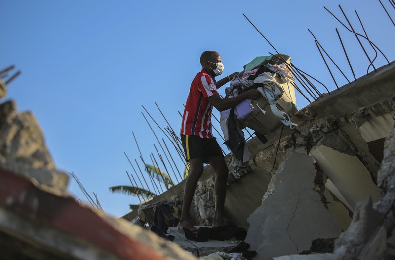 People walk past a home destroyed by the earthquake in Les Cayes, Haiti, Saturday, Aug. 14, 2021. A 7.2 magnitude earthquake struck Haiti on Saturday, with the epicenter about 125 kilometers (78 miles) west of the capital of Port- au-Prince, the US Geological Survey said. (AP Photo/Joseph Odelyn)