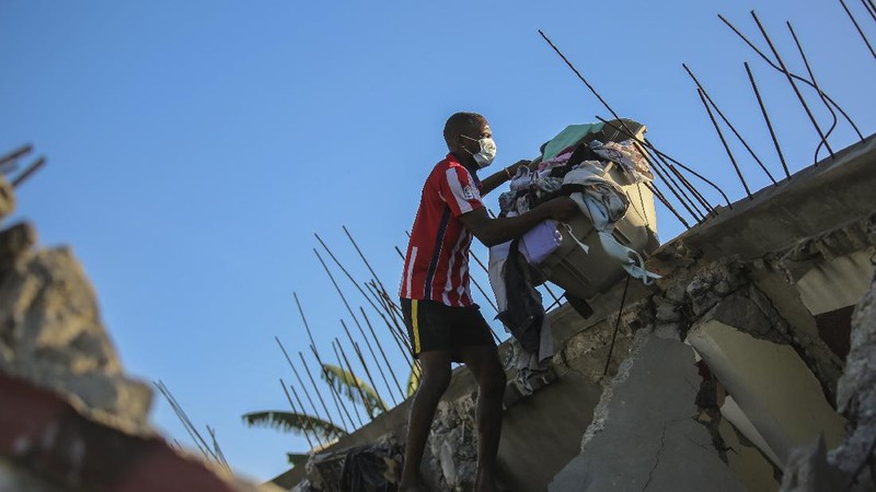 People walk past a home destroyed by the earthquake in Les Cayes, Haiti, Saturday, Aug. 14, 2021. A 7.2 magnitude earthquake struck Haiti on Saturday, with the epicenter about 125 kilometers (78 miles) west of the capital of Port- au-Prince, the US Geological Survey said. (AP Photo/Joseph Odelyn)