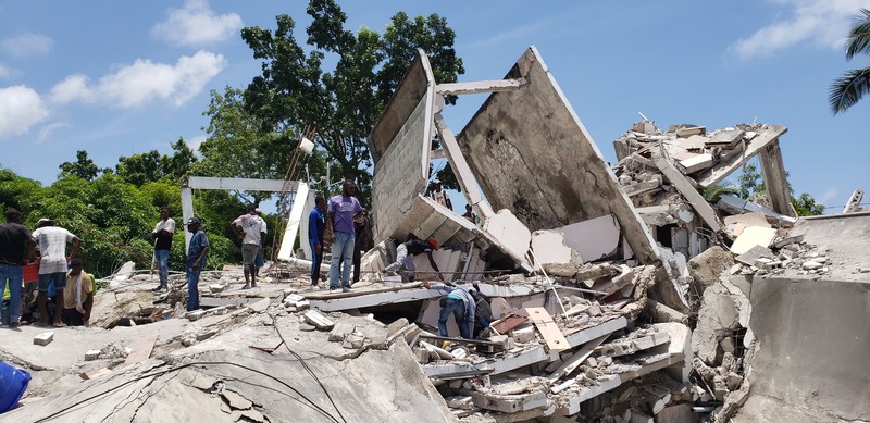 People walk past a home destroyed by the earthquake in Les Cayes, Haiti, Saturday, Aug. 14, 2021. A 7.2 magnitude earthquake struck Haiti on Saturday, with the epicenter about 125 kilometers (78 miles) west of the capital of Port- au-Prince, the US Geological Survey said. (AP Photo/Joseph Odelyn)