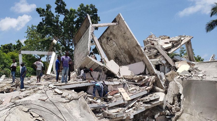 People walk past a home destroyed by the earthquake in Les Cayes, Haiti, Saturday, Aug. 14, 2021. A 7.2 magnitude earthquake struck Haiti on Saturday, with the epicenter about 125 kilometers (78 miles) west of the capital of Port- au-Prince, the US Geological Survey said. (AP Photo/Joseph Odelyn)