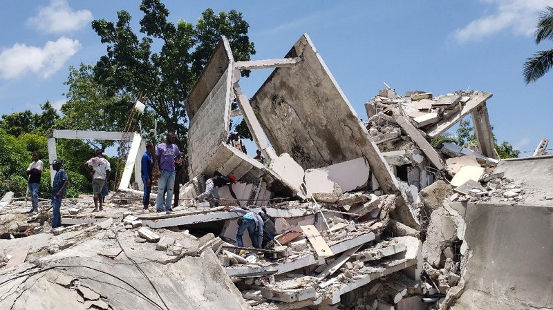 People walk past a home destroyed by the earthquake in Les Cayes, Haiti, Saturday, Aug. 14, 2021. A 7.2 magnitude earthquake struck Haiti on Saturday, with the epicenter about 125 kilometers (78 miles) west of the capital of Port- au-Prince, the US Geological Survey said. (AP Photo/Joseph Odelyn)