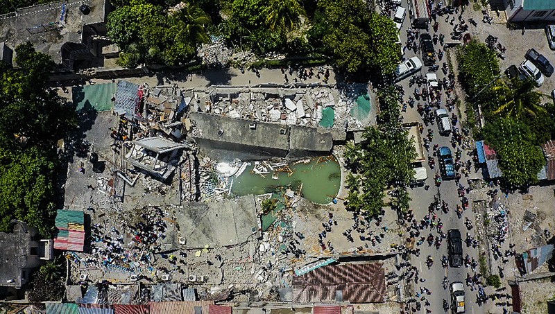 People walk past a home destroyed by the earthquake in Les Cayes, Haiti, Saturday, Aug. 14, 2021. A 7.2 magnitude earthquake struck Haiti on Saturday, with the epicenter about 125 kilometers (78 miles) west of the capital of Port- au-Prince, the US Geological Survey said. (AP Photo/Joseph Odelyn)