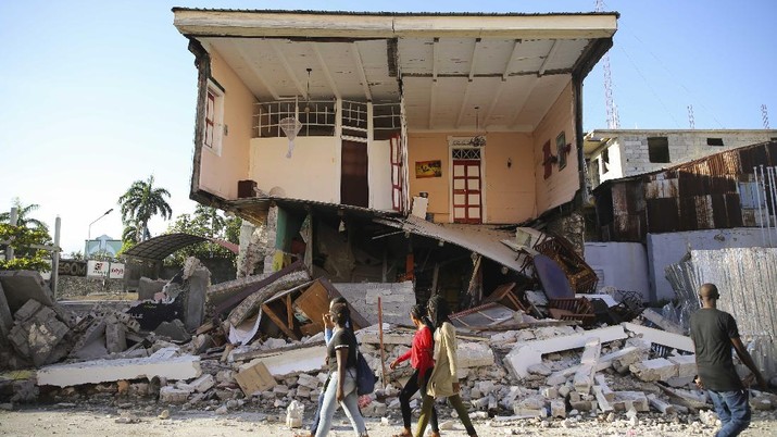 People walk past a home destroyed by the earthquake in Les Cayes, Haiti, Saturday, Aug. 14, 2021. A 7.2 magnitude earthquake struck Haiti on Saturday, with the epicenter about 125 kilometers (78 miles) west of the capital of Port- au-Prince, the US Geological Survey said. (AP Photo/Joseph Odelyn)