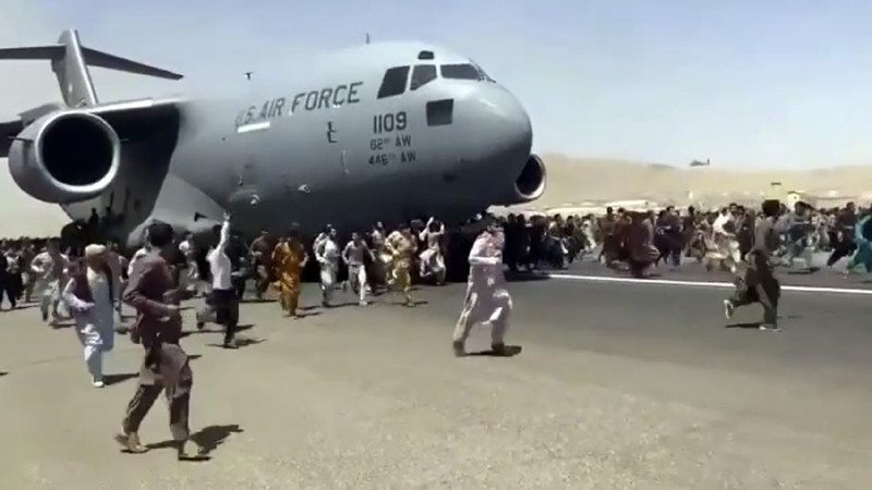 Hundreds of people run alongside a U.S. Air Force C-17 transport plane as it moves down a runway of the international airport, in Kabul, Afghanistan, Monday, Aug.16. 2021. Thousands of Afghans have rushed onto the tarmac at the airport, some so desperate to escape the Taliban capture of their country that they held onto the American military jet as it took off and plunged to death. (Verified UGC via AP)