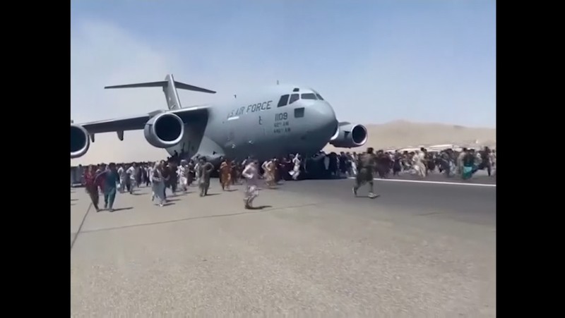 Hundreds of people run alongside a U.S. Air Force C-17 transport plane as it moves down a runway of the international airport, in Kabul, Afghanistan, Monday, Aug.16. 2021. Thousands of Afghans have rushed onto the tarmac at the airport, some so desperate to escape the Taliban capture of their country that they held onto the American military jet as it took off and plunged to death. (Verified UGC via AP)