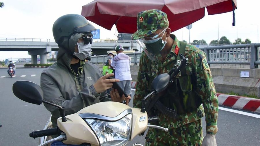 An army soldier checks identifications at a COVID-19 lockdown checkpoint in Ho Chi Minh City, Vietnam, Monday, Aug. 23, 2021. Vietnam's largest metropolis Ho Chi Minh City has enabled a strict lockdown order to help curb the recent outbreak of the pandemic. (Vu Tien Luc/VNA via AP)