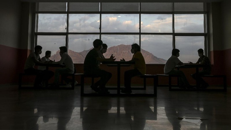 A security official checks migrants, mainly coming from Afghanistan, queue for lunch at a deportation center in Turkish city of Van that borders Iran, Turkey, Sunday. Aug. 22, 2021. Traffic on this key migration route from central Asia to Europe has remained relatively stable compared to previous years. But European countries, as well as Turkey, fear the sudden return of Taliban rule in Afghanistan could change that.(AP Photo/Emrah Gurel)