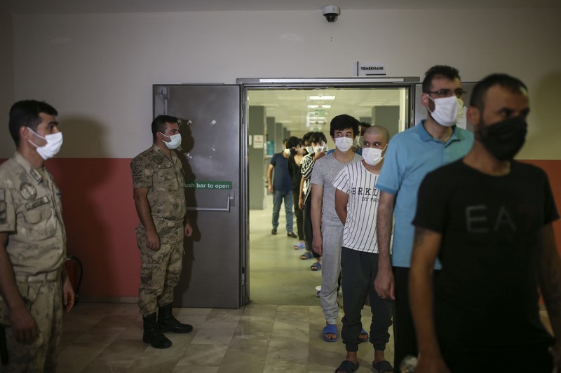 Turkey Afghanistan A security official checks migrants, mainly coming from Afghanistan, queue for lunch at a deportation center in Turkish city of Van that borders Iran, Turkey, Sunday. Aug. 22, 2021. Traffic on this key migration route from central Asia to Europe has remained relatively stable compared to previous years. But European countries, as well as Turkey, fear the sudden return of Taliban rule in Afghanistan could change that.(AP Photo/Emrah Gurel)