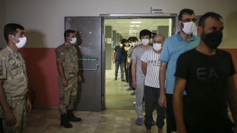 A security official checks migrants, mainly coming from Afghanistan, queue for lunch at a deportation center in Turkish city of Van that borders Iran, Turkey, Sunday. Aug. 22, 2021. Traffic on this key migration route from central Asia to Europe has remained relatively stable compared to previous years. But European countries, as well as Turkey, fear the sudden return of Taliban rule in Afghanistan could change that.(AP Photo/Emrah Gurel)