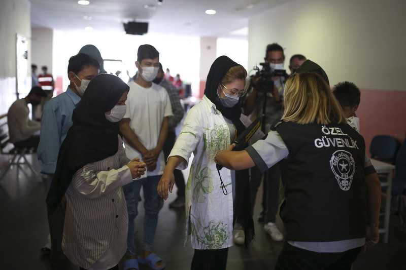 Turkey Afghanistan A security official checks migrants, mainly coming from Afghanistan, queue for lunch at a deportation center in Turkish city of Van that borders Iran, Turkey, Sunday. Aug. 22, 2021. Traffic on this key migration route from central Asia to Europe has remained relatively stable compared to previous years. But European countries, as well as Turkey, fear the sudden return of Taliban rule in Afghanistan could change that.(AP Photo/Emrah Gurel)