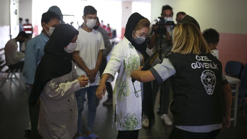 A security official checks migrants, mainly coming from Afghanistan, queue for lunch at a deportation center in Turkish city of Van that borders Iran, Turkey, Sunday. Aug. 22, 2021. Traffic on this key migration route from central Asia to Europe has remained relatively stable compared to previous years. But European countries, as well as Turkey, fear the sudden return of Taliban rule in Afghanistan could change that.(AP Photo/Emrah Gurel)