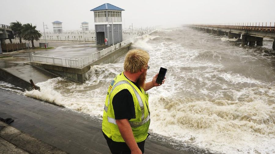 A utility worker photographs waves as they slam against a sea wall at the city marina as outer bands of Hurricane Ida arrive Sunday, Aug. 29, 2021, in Bay Saint Louis, Miss. (AP Photo/Steve Helber)