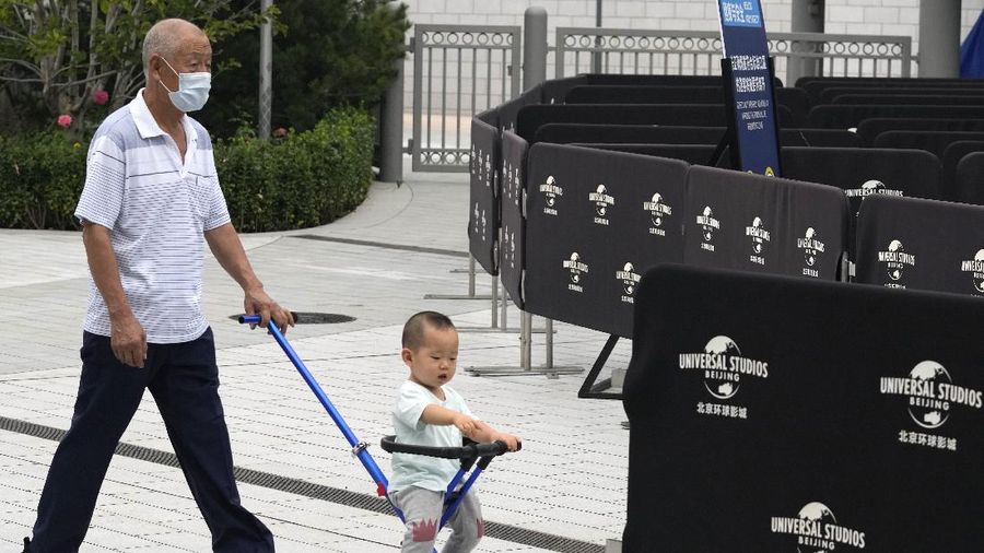 An elderly man pushes a child near barricades outside the Universal Studios theme park during trial runs in Beijing, China, Tuesday, Aug. 31, 2021. Universal Studios announced Monday, Aug. 30, 2021, that its first theme park in China will open in the country's capital in September. The company set the opening date for Sept. 20, according to a statement and video posted on the Chinese social media site WeChat. (AP Photo/Ng Han Guan)