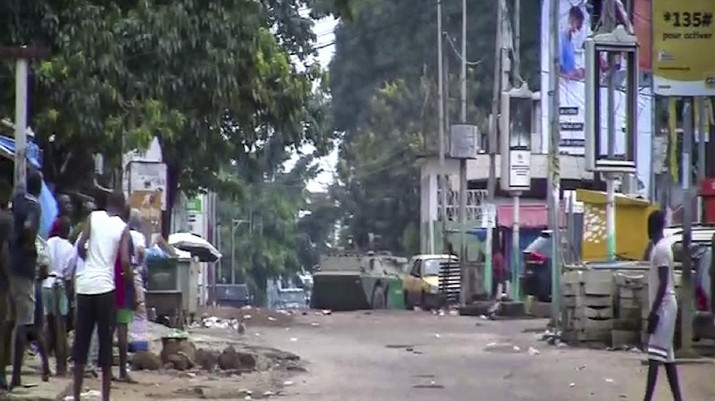 In this image made from video, residents watch as an armored personnel carrier is seen on the streets near the presidential palace in the capital Conakry, Guinea Sunday, Sept. 5, 2021. Mutinous soldiers detained President Alpha Conde on Sunday after hours of heavy gunfire rang out near the presidential palace, then announced on state television that the government had been dissolved in an apparent coup d'etat. (AP Photo)