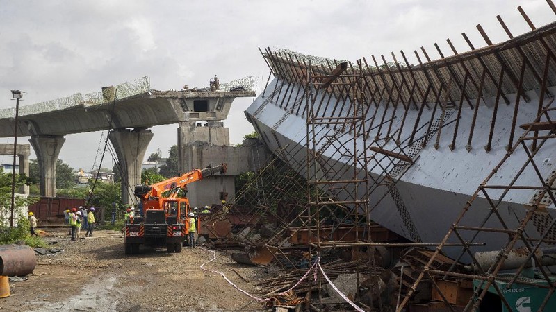 Workers stand near an under-construction bridge that collapsed in Mumbai, India, Friday, Sept. 17, 2021. According to police more than a dozen people were injured after a part of the under-construction bridge collapsed early Friday morning in Mumbai. (AP Photo/Rafiq Maqbool)