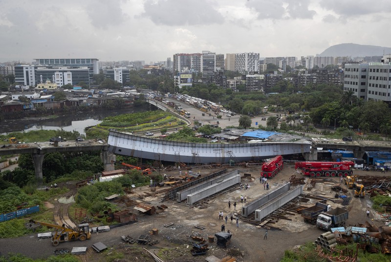 Workers stand near an under-construction bridge that collapsed in Mumbai, India, Friday, Sept. 17, 2021. According to police more than a dozen people were injured after a part of the under-construction bridge collapsed early Friday morning in Mumbai. (AP Photo/Rafiq Maqbool)