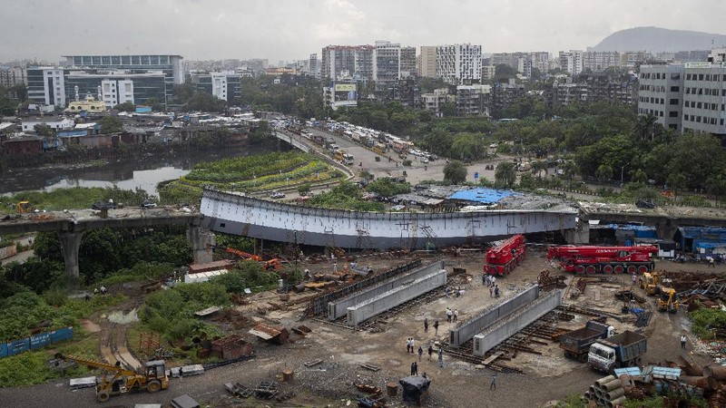 Workers stand near an under-construction bridge that collapsed in Mumbai, India, Friday, Sept. 17, 2021. According to police more than a dozen people were injured after a part of the under-construction bridge collapsed early Friday morning in Mumbai. (AP Photo/Rafiq Maqbool)