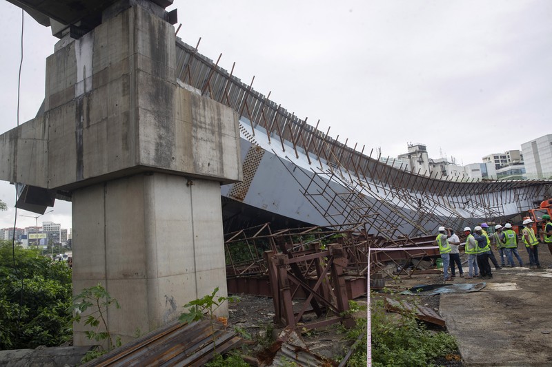 Workers stand near an under-construction bridge that collapsed in Mumbai, India, Friday, Sept. 17, 2021. According to police more than a dozen people were injured after a part of the under-construction bridge collapsed early Friday morning in Mumbai. (AP Photo/Rafiq Maqbool)