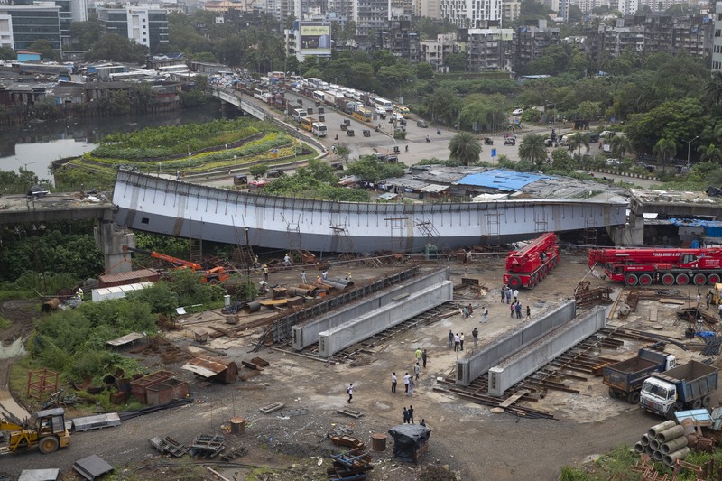 Workers stand near an under-construction bridge that collapsed in Mumbai, India, Friday, Sept. 17, 2021. According to police more than a dozen people were injured after a part of the under-construction bridge collapsed early Friday morning in Mumbai. (AP Photo/Rafiq Maqbool)