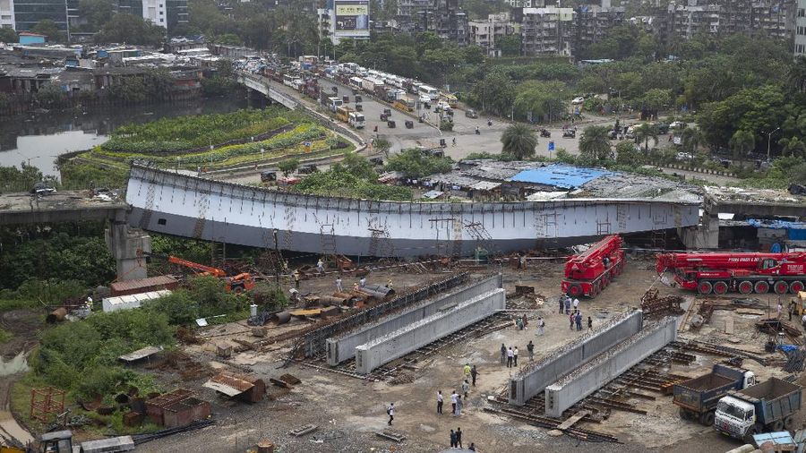 Workers stand near an under-construction bridge that collapsed in Mumbai, India, Friday, Sept. 17, 2021. According to police more than a dozen people were injured after a part of the under-construction bridge collapsed early Friday morning in Mumbai. (AP Photo/Rafiq Maqbool)