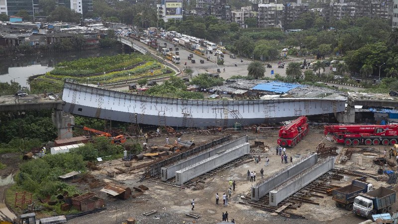 Workers stand near an under-construction bridge that collapsed in Mumbai, India, Friday, Sept. 17, 2021. According to police more than a dozen people were injured after a part of the under-construction bridge collapsed early Friday morning in Mumbai. (AP Photo/Rafiq Maqbool)