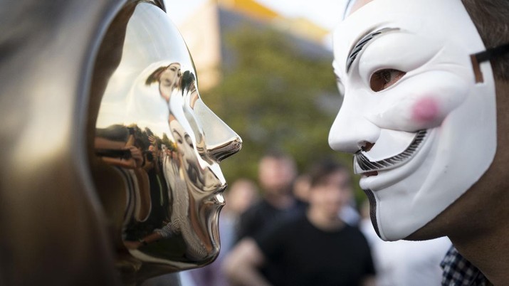 A man wearing a a Guy Fawkes mask looks at a newly unveiled statue of the mysterious developer of the Bitcoin digital currency in Budapest, Hungary, Thursday, Sept. 16, 2021. A bronze statue was unveiled in Hungary’s capital on Thursday which its creators say is the first in the world to pay homage to the anonymous creator of the Bitcoin digital currency. Erected in a business park near the Danube River in Budapest, the bust sits atop a stone plinth engraved with the name of Satoshi Nakamoto, the pseudonym of the mysterious developer of Bitcoin whose true identity is unknown. (AP Photo/Bela Szandelszky)
