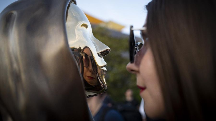 A man wearing a a Guy Fawkes mask looks at a newly unveiled statue of the mysterious developer of the Bitcoin digital currency in Budapest, Hungary, Thursday, Sept. 16, 2021. A bronze statue was unveiled in Hungary’s capital on Thursday which its creators say is the first in the world to pay homage to the anonymous creator of the Bitcoin digital currency. Erected in a business park near the Danube River in Budapest, the bust sits atop a stone plinth engraved with the name of Satoshi Nakamoto, the pseudonym of the mysterious developer of Bitcoin whose true identity is unknown. (AP Photo/Bela Szandelszky)