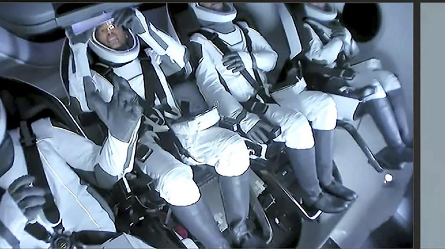 In this combination of split screen images taken from SpaceX video, passengers aboard a SpaceX capsule, left, react as the capsule, right, parachutes into the Atlantic Ocean off the Florida coast, Saturday, Sept. 18, 2021. The all-amateur crew was the first to circle the world without a professional astronaut.  (SpaceX via AP)