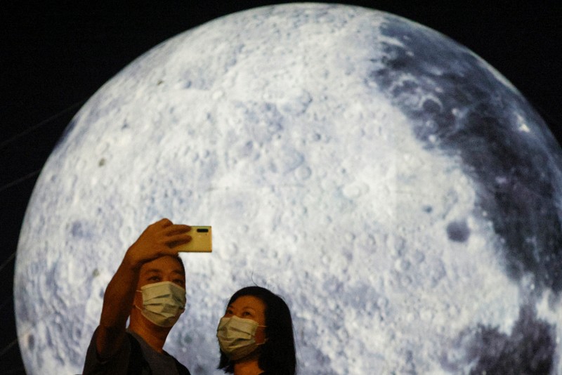 Seorang wanita berpose di depan balon raksasa berbentuk bulan menjelang Festival Pertengahan Musim Gugur, di Hong Kong, China 20 September 2021. (REUTERS/Tyrone Siu) A woman poses for a photo in front of a giant moon-shaped balloon ahead of Mid-Autumn Festival, in Hong Kong, China September 20, 2021. REUTERS/Tyrone Siu
