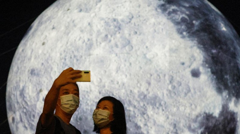 A woman poses for a photo in front of a giant moon-shaped balloon ahead of Mid-Autumn Festival, in Hong Kong, China September 20, 2021. REUTERS/Tyrone Siu