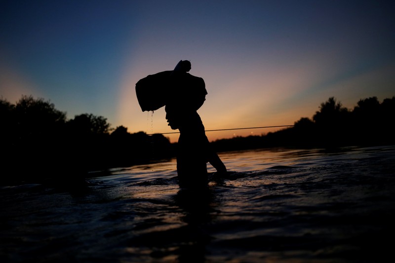 Migrants seeking refuge in the United States walk back into the Mexican side carrying their belongings inside plastic bags while crossing the Rio Bravo river which divides the border between Ciudad Acuna, Mexico and Del Rio, Texas, U.S., to avoid being deported, in Ciudad Acuna, Mexico, September 19, 2021. REUTERS/Daniel Becerril   REFILE- QUALITY REPEAT