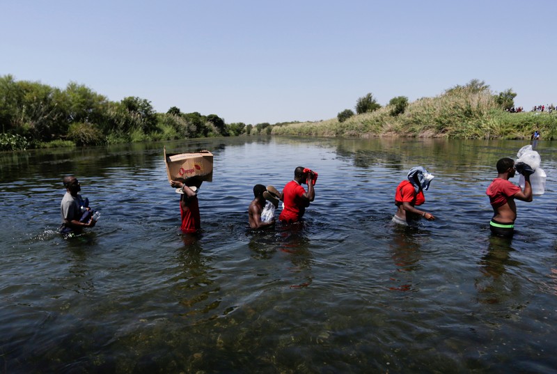 Migrants seeking refuge in the United States walk back into the Mexican side carrying their belongings inside plastic bags while crossing the Rio Bravo river which divides the border between Ciudad Acuna, Mexico and Del Rio, Texas, U.S., to avoid being deported, in Ciudad Acuna, Mexico, September 19, 2021. REUTERS/Daniel Becerril   REFILE- QUALITY REPEAT